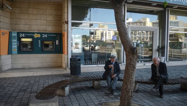 Пожилые жители Никосии сидят на лавочке у банкоматов Cyprus Popular Bank (CPB)