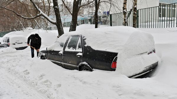 Мужчина очищает занесенный снегом автомобиль