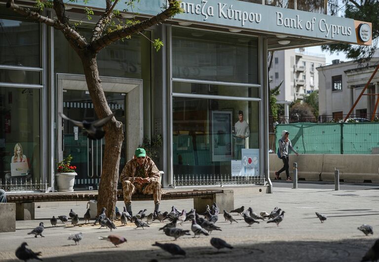 Мужчина кормит голубей у закрытого офиса Bank of Cyprus в Никосии Мужчина кормит голубей у закрытого офиса Bank of Cyprus в Никосии
