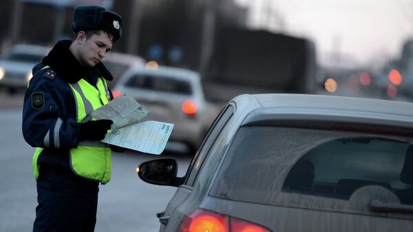 Сотрудник дорожно-патрульной службы ГИБДД проверяет документы у водителя автомобиля