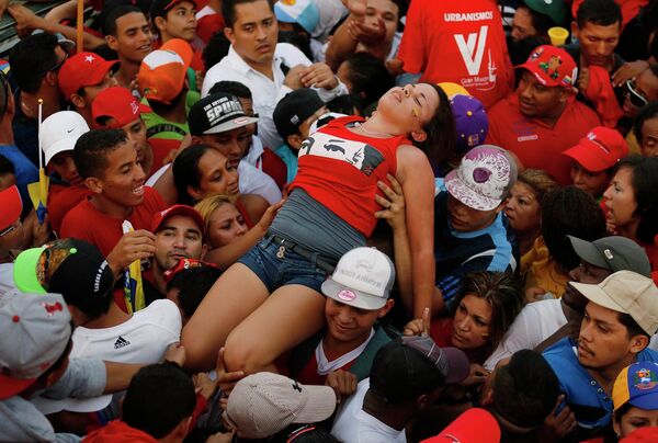 Сторонники Николаса Мадуро выносят из толпы девушку, упавшую в обморок на предвыборном митинге в Каракасе