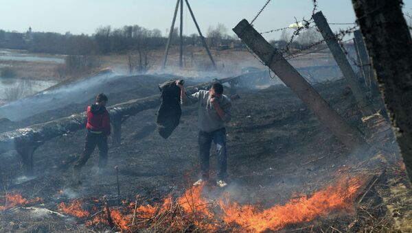 Молодой человек пытается потушить очаг возгорания сухой травы. Архивное фото