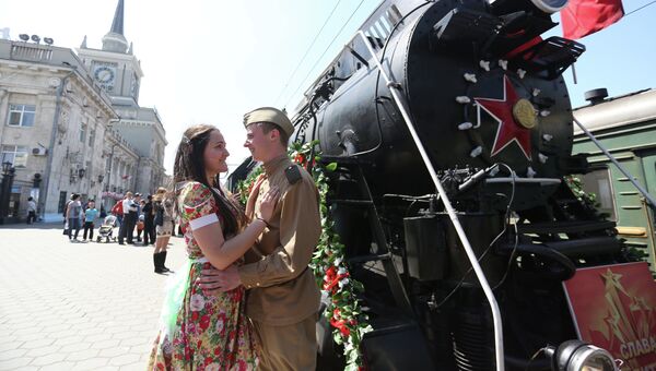 Молодые люди в одежде времен Великой Отечественной войны стоят у ретро-поезда Победа