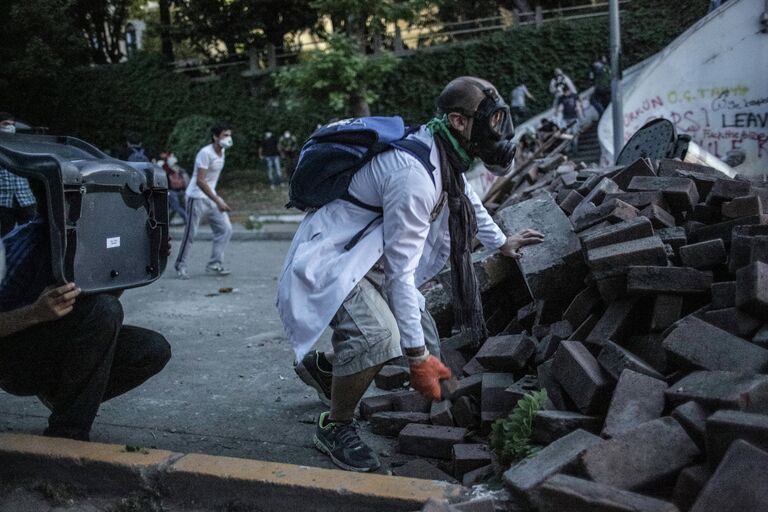 Один из протестующих прячется за баррикадой во время столкновения с сотрудниками полиции в Стамбуле