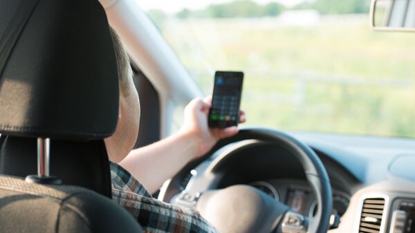 Молодой человек пользуется мобильным телефоном за рулем автомобиля