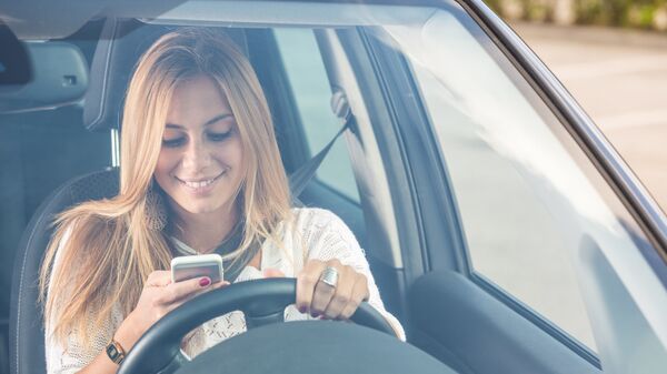 Девушка пользуется мобильным телефоном за рулем автомобиля