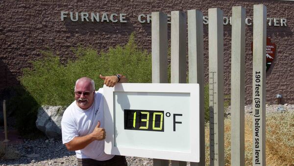 Сотрудник центра для туристов города Фёрнес-Крик возле термометра в Долине Смерти в Калифорнии. На термометре 54,4 градуса по Цельсию