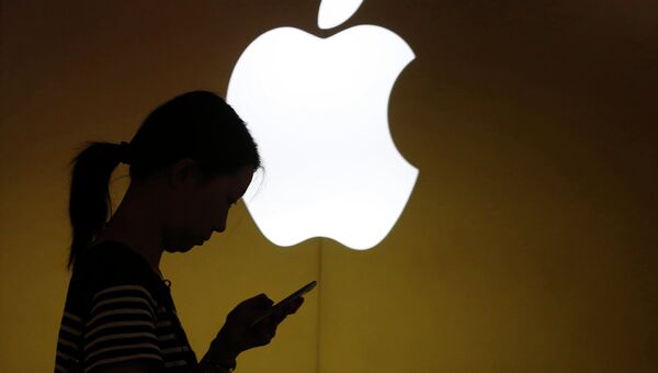 Женщина смотрит на экран мобильного телефона на фоне логотипа компании Apple, архивное фото