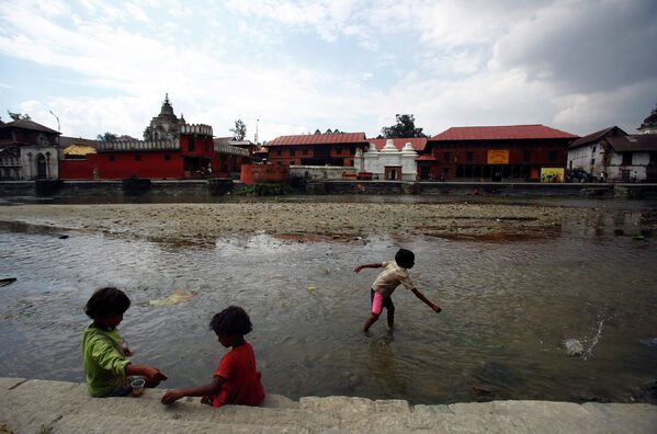 Дети ищут монеты с помощью магнита в реке Багмати, протекающей через храм Пашупатинатх в Катманду
