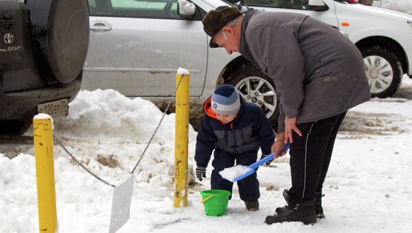 Ребенок вместе с дедушкой играет со снегом на улице, архивное фото