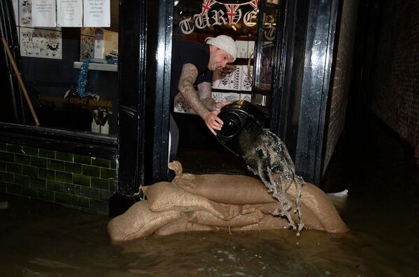 Владелец тату-салона выгребает воду во время шторма в Уитби, на севере Англии