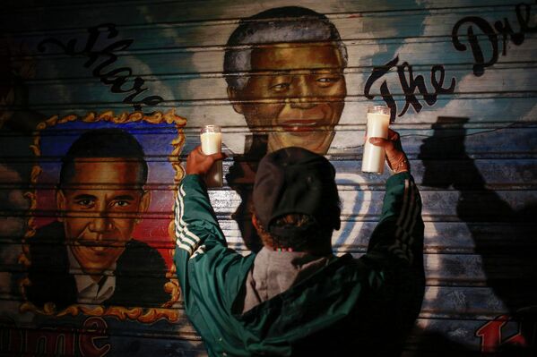 Мужчина держит свечи перед фреской с изображением экс-президента ЮАР Нельсона Манделы