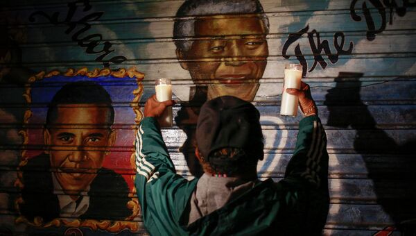 Мужчина держит свечи перед фреской с изображением экс-президента ЮАР Нельсона Манделы