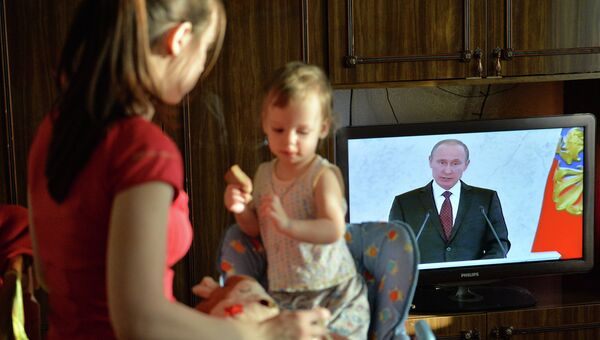 Молодая мама кормит ребенка во время просмотра трансляции обращения президента Владимира Путина. Архивное фото