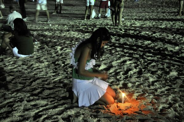 Девушка на пляже зажигает свечу на Новый год в Бразилии