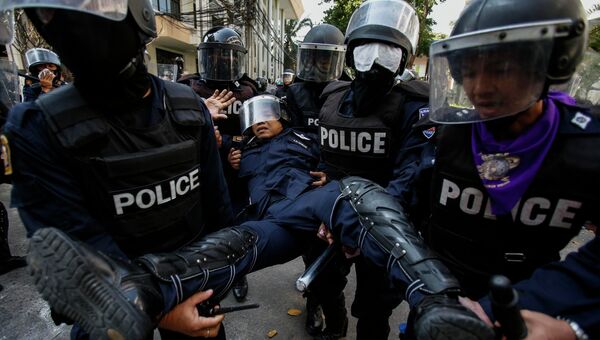 Полиция выносит раненого сослуживца во время беспорядков в Бангкоке. 26 декабря 2013