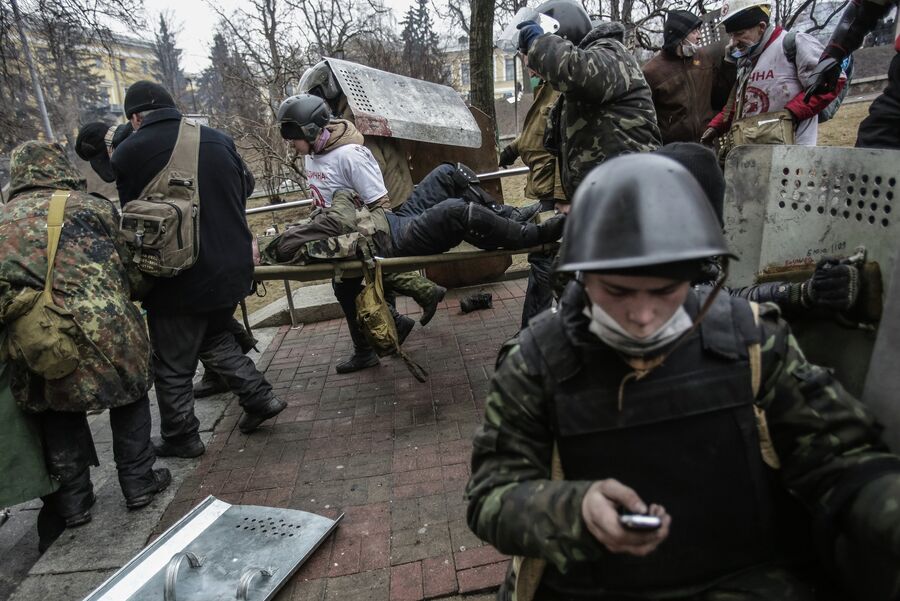 Сторонники оппозиции несут раненного во время столкновений с сотрудниками правопорядка в Киеве