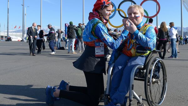 Волонтер в Олимпийском парке Сочи рисует на щеке болельщика российский флаг