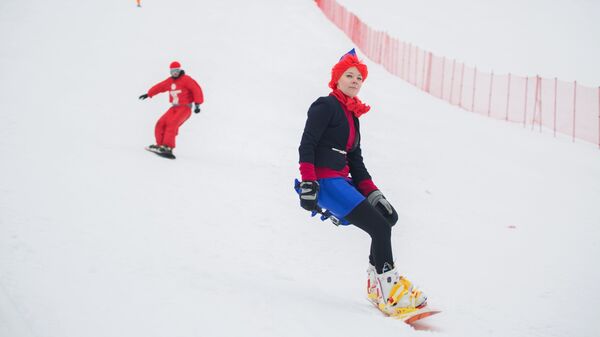 Девушка в костюме стюардессы, участвующая в Снежном карнавале, спускается на сноуборде по склону Запад на территории горнолыжного комплекса Горный воздух в Южно-Сахалинске