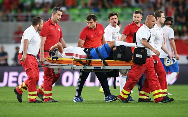 Медики уносят с поля получившего травму полузащитника сборной России Романа Зобнина