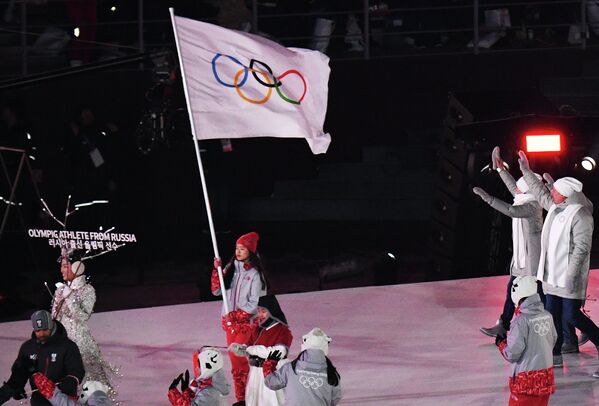Волонтер несет олимпийский флаг и олимпийские атлеты из России