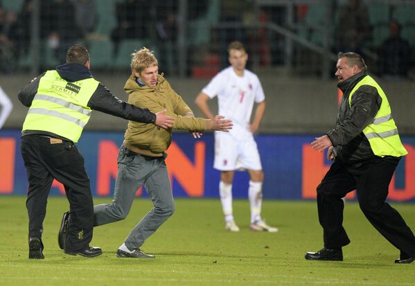 Сотрудники стадиона задерживают молодого человека, выбежавшего на поле во время матча Люксембург - Россия
