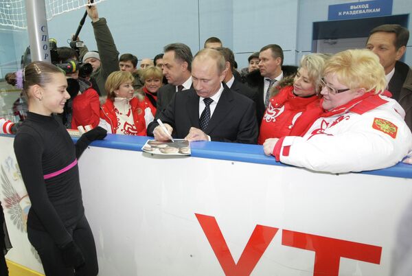 Председатель правительства РФ Владимир Путин (в центре на первом плане) дает автограф фигуристке Аделине Сотниковой (слева на первом плане)