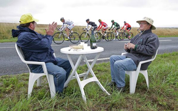 Двое болельщиков за обедом наблюдают за группой велогонщиков на седьмом этапе Тур де Франс