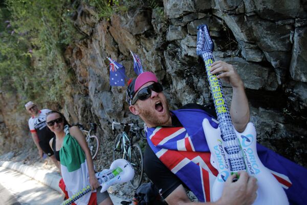 Зритель, завернутый в Австралийский флаг играет на гитаре в ожидании велогонщик на участке семнадцатого этапа Тур де Франс между городами Сен-Годан и Сен-Лари