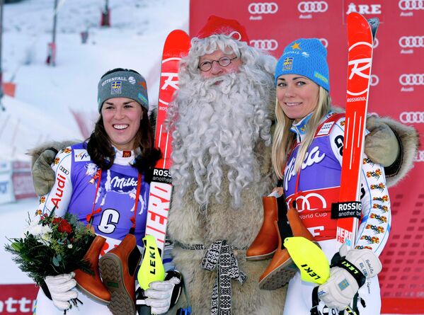 Шведские горнолыжницы Мария Пиетиля-Хольмнер и Фриде Хансдоттер с Санта-Клаусом на подиуме этапе Кубка мира в Оре