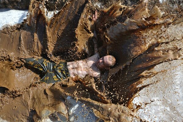 Участник соревнований Грязный забег принимает грязевые ванны после забега по берегу реки Казанки