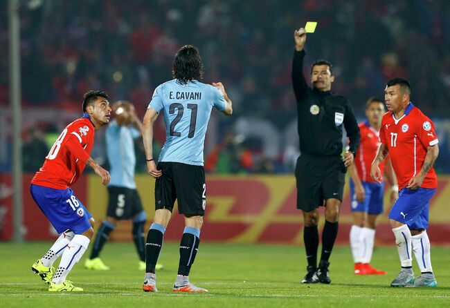 Главный арбитр матча Кубка Америки между сборными Чили и Уругвая Сандро Риччи (в центре) показывает желтую карточку форворду уругвайцев Эдинсону Кавани (слева)