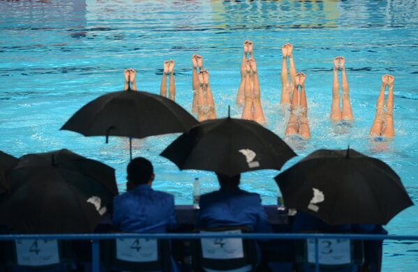 Судейская бригада наблюдает за выступлением в произвольной программе в комбинации команды сборной КНДР на соревнованиях по синхронному плаванию