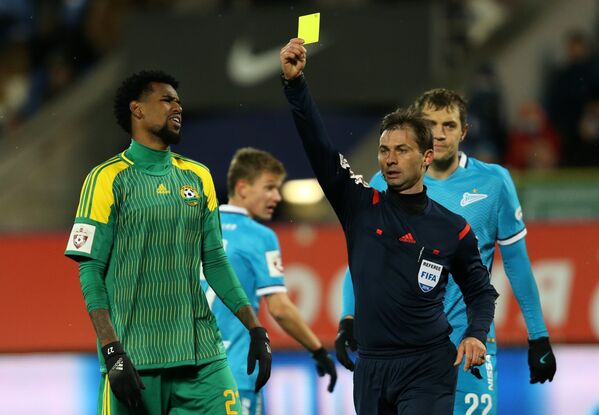 Главный судья матча Алексей Еськов показывает желтую карточку защитнику Кубани Фелипе Сантана (слева)
